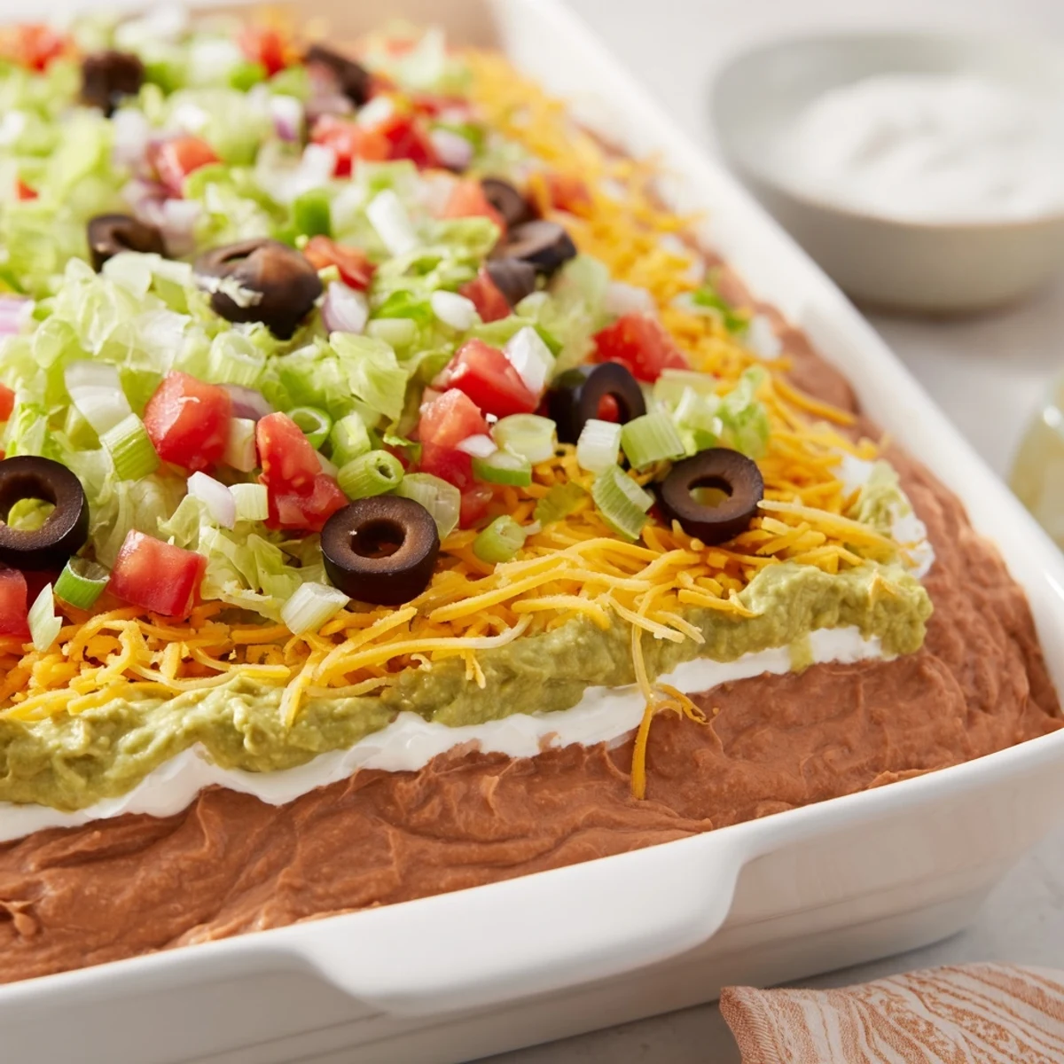 A layered Seven-Layer Dip appetizer with vibrant colors, perfect with crispy tortilla chips for snacking.
