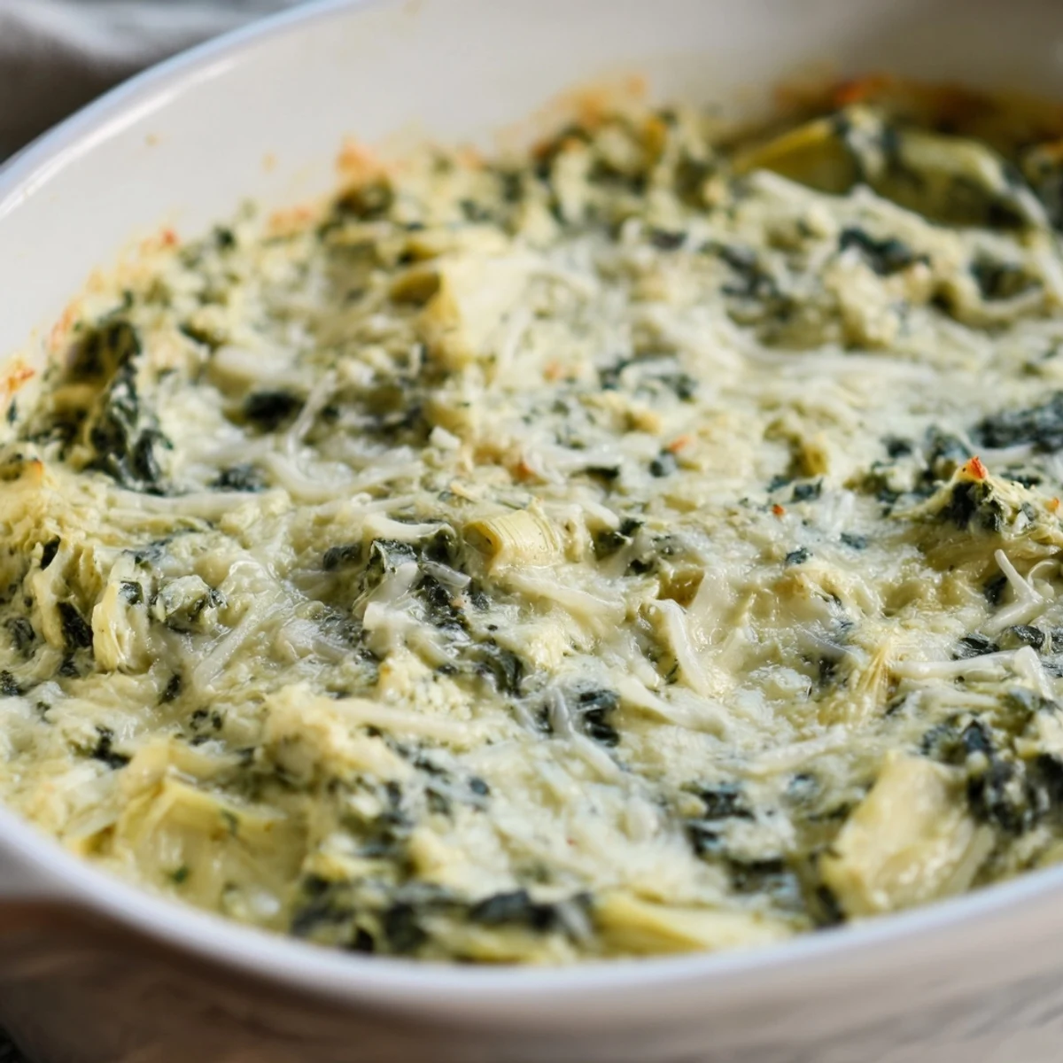 Creamy, bubbling Spinach Artichoke Dip, golden-brown on top, ready for dipping on the table.