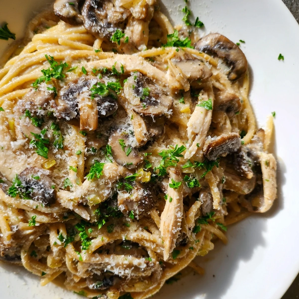 Steaming Creamy Mushroom Chicken Spaghettini served in a white bowl, garnished with fresh parsley and grated Parmesan.  