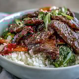 Teriyaki beef bowl features glossy glazed beef, crisp vegetables, and steamed rice, garnished with sesame seeds and scallions.  