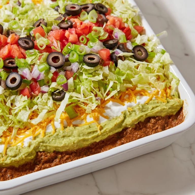 Enjoy the delicious, chilled Seven-Layer Dip, a Tex-Mex classic with flavorful refried beans and guacamole.