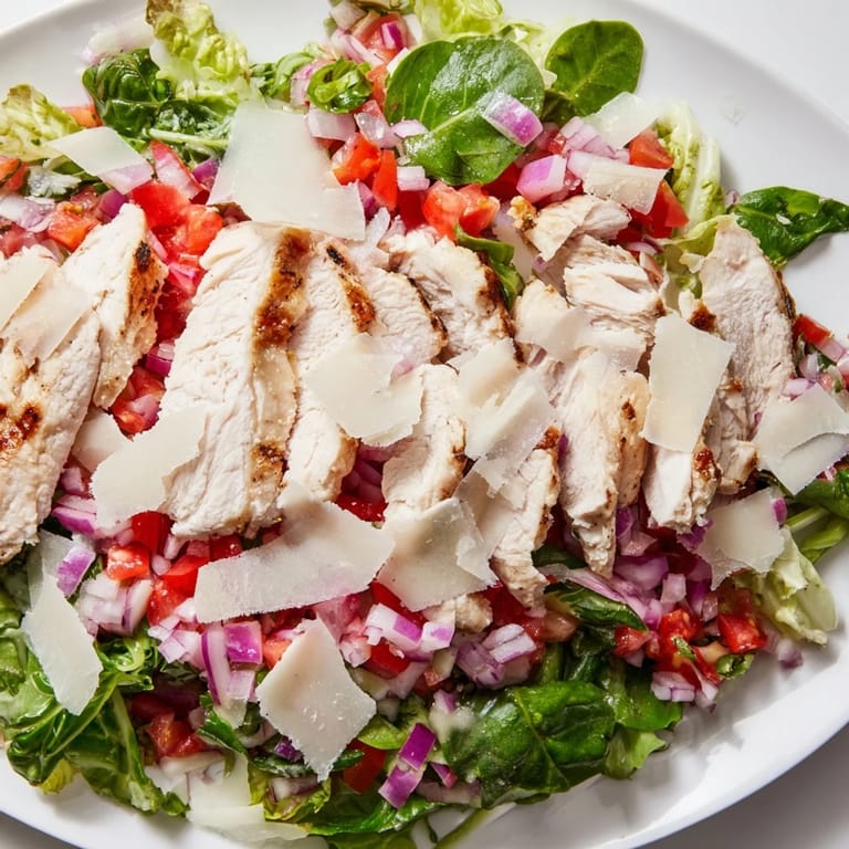 A colorful Bruschetta Chicken Salad plated on a white dish, featuring vibrant red tomatoes, green basil, and golden grilled chicken.