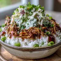 Tender, slow-cooked pulled pork piled high over fluffy white rice in a colorful bowl, topped with creamy tangy coleslaw and a rich BBQ sauce drizzle.  
