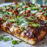 Smoky BBQ chicken flatbread pizza with melty mozzarella, red onion, and bell pepper, garnished with fresh cilantro and a BBQ drizzle.  